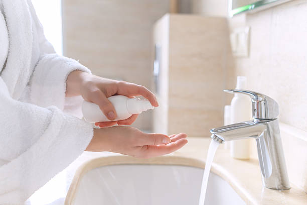 istock Woman in the robe washing hands using liquid soap or antibacterial gel for protective and care dry skin near white sink in bathroom with sunlight from the window. 2207607669