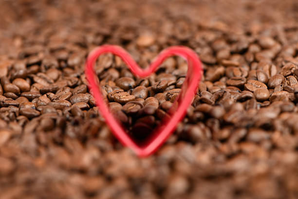 Red heart in roasted coffee beans background. High resolution photo. Soft focus.