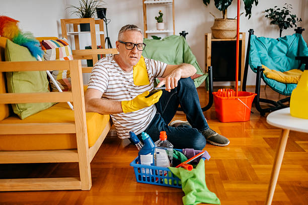 istock Mid adult man cleaning his home and taking a break while using mobile phone 2207612238