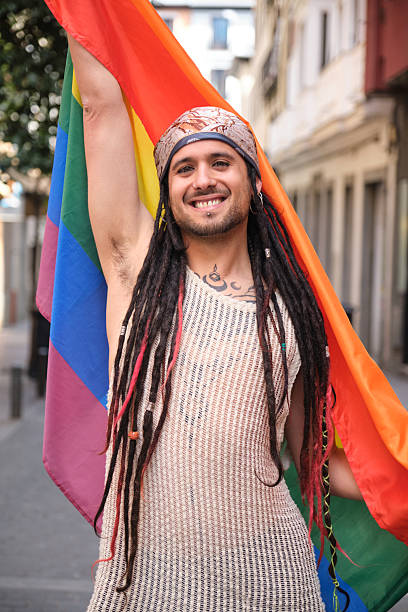 istock Young man with dreadlocks holding rainbow flag smiling at camera 2207623492