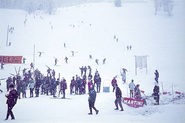 Vorarlberg, Austria, 1964. Ski slalom event with participants, helpers, and spectators in the foothills of the Alps during snowfall.