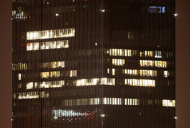 People are working overtime in brightly lit office buildings late at night