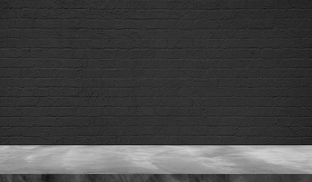 istock empty grey plaster concrete table top in foreground with dark black plaster brick wall at background. counter bar foreground can be used for display. 2207642949