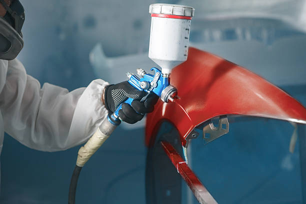 istock Car paint worker spraying red paint to car body element using spray gun in vehicle workshop chamber. Complex restoration of automobile body. 2207643249