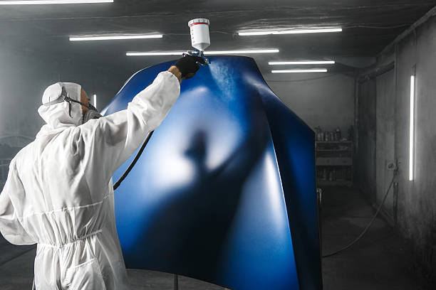 istock Professional bodywork, male car painter in protective mask and workwear apply few layer paint from spray gun to automobile body parts in garage booth. 2207643416