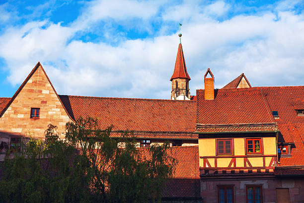 Charming Nuremberg old town with tiled roofs and a mix of stone and timber-framed buildings that evoke a sense of history. Cloudy sky serve as picturesque backdrop, enhancing timeless appeal of scene