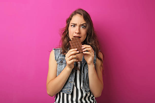 istock Portrait of young woman with chocolate bar on pink background 2207650737