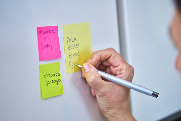 istock Writting Shopping List on Adhesive Note and Putting on Refrigirator 2207653999