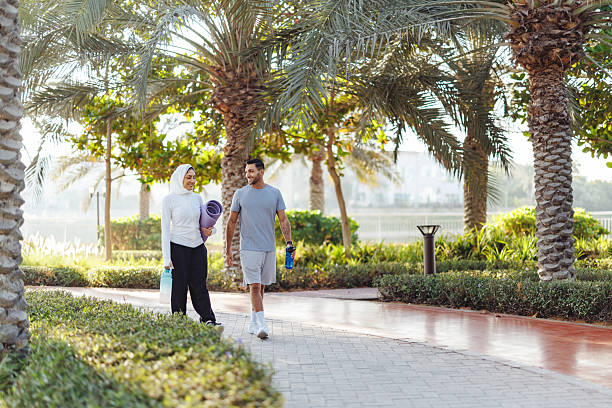 Mixed Race Couple Walking On Palm-Lined Path After Morning Workout In Dubai Park