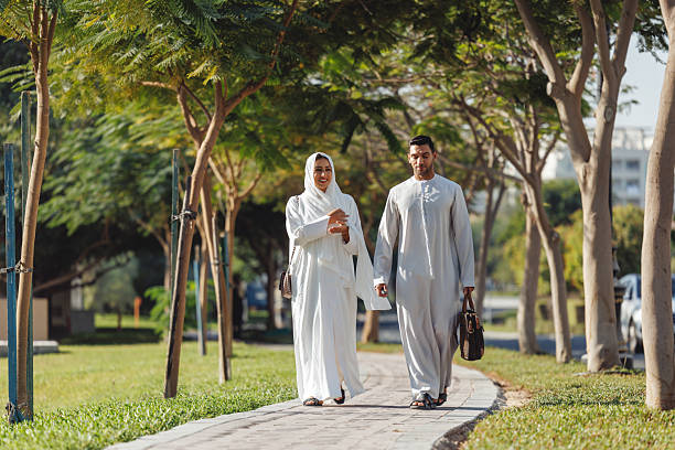 istock Middle Eastern Couple In Traditional White Attire Walking Through Tree-Lined Park Path In Dubai 2207665092