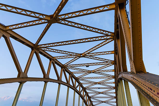 A detailed view of a bridge's metal framework displays the intricacies of its design, highlighted by the soft morning light and a clear blue sky, showcasing engineering precision.