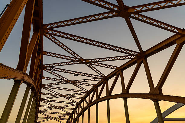 A detailed view of a bridge's metal framework displays the intricacies of its design, highlighted by the soft morning light and a clear blue sky, showcasing engineering precision.