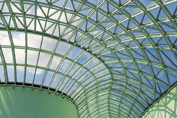 The intricate design of a glass roof reveals a metal framework beneath, capturing the bright blue sky and daylight filtering through, showcasing modern architectural beauty.Architectural detail of the roof of Galeria Katowicka - shopping, entertainment, and office center, located in Katowice, Poland.