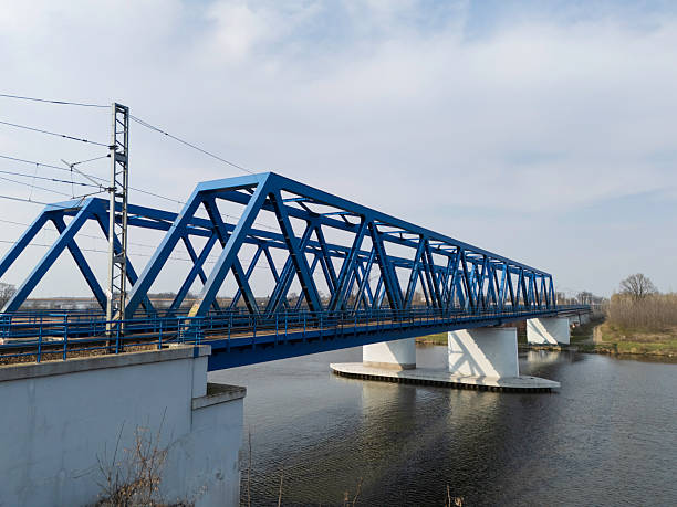 A well-structured blue metal bridge spans over a body of water, displaying intricate details of rail tracks positioned below. The view highlights modern engineering.