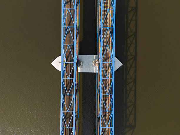 A well-structured blue metal bridge spans over a body of water, displaying intricate details of rail tracks positioned below. The view highlights modern engineering.