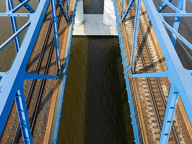 A well-structured blue metal bridge spans over a body of water, displaying intricate details of rail tracks positioned below. The view highlights modern engineering.