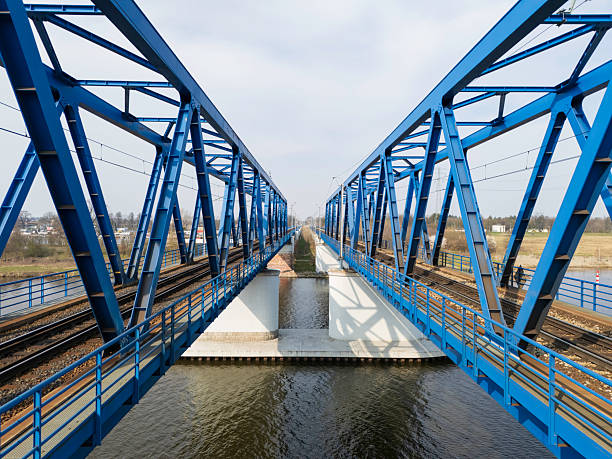 A well-structured blue metal bridge spans over a body of water, displaying intricate details of rail tracks positioned below. The view highlights modern engineering.