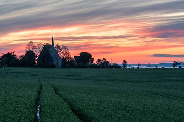 Scenic sunset over a rural landscape with a church silhouette and vibrant sky, capturing serene beauty and tranquility.