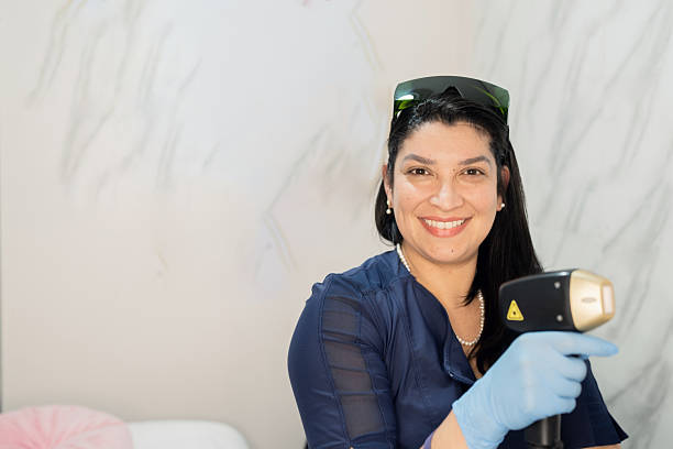 Beautician wearing gloves and protective glasses holding a laser epilator device and smiling