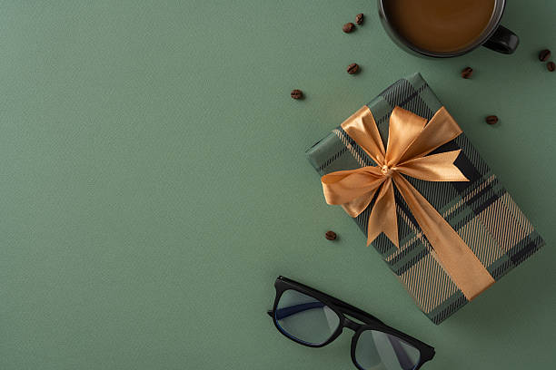 istock Stylish gift box wrapped with bow sitting on green surface next to cup of coffee and sunglasses, suggesting a celebration, appreciation, or thoughtful moment for a special occasion 2207690370