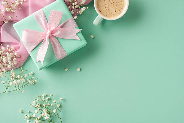 istock Pastel-colored gift box adorned with a ribbon surrounded by flowers, with a coffee cup on a matching green background. A composition representing care, celebration, and thoughtful presents 2207690387