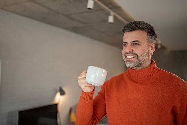 istock Smiling man drinking coffee at home in modern living room 2207691311