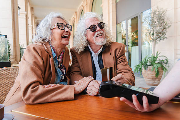 istock Joyful elderly couple enjoying a delightful moment while happily making a credit card payment at a charming outdoor cafe filled with laughter and shared memories in a delightful atmosphere 2207699172
