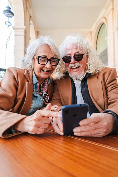 istock Joyful senior couple enjoying a delightful moment together while using a smartphone to explore apps and share laughter in a cozy outdoor cafe atmosphere with warm smiles and genuine connection 2207699320