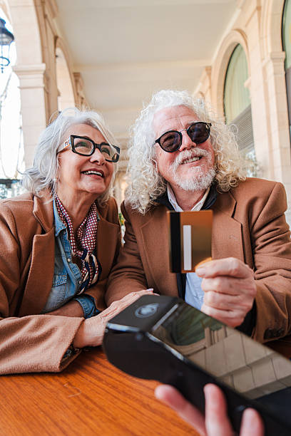 istock Joyful senior couple happily making a payment with a credit card while smiling and enjoying their time together at a charming cafe table in a delightful outdoor setting with a payment terminal 2207699485