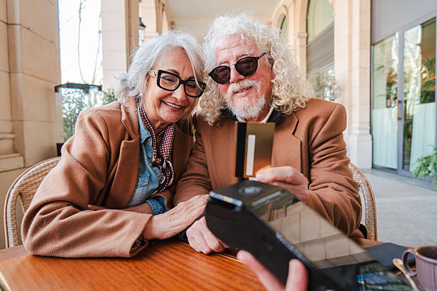 istock Elderly couple joyfully sharing a moment while making a payment with a credit card at a cozy table in a lively cafe, showcasing their love and connection in the delightful act of spending time together 2207700209