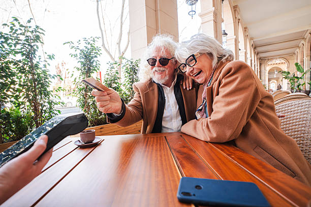 istock Elderly couple joyfully sharing a moment while using a smartphone to capture their delightful experience at a cozy cafe, showcasing their warm connection and love for technology and each other 2207700452