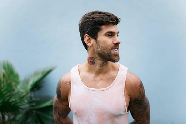Portrait of a happy young man with tattoos and beard wearing tank top and looking away