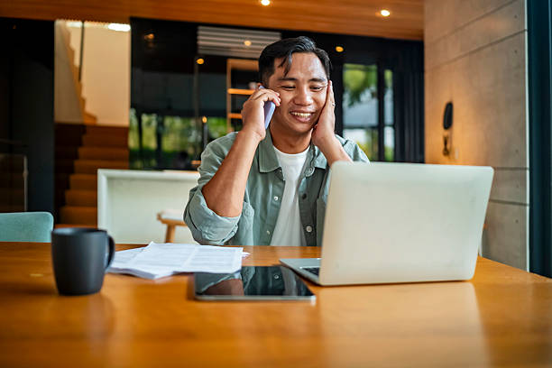 istock Smiling Man Working From Home on Laptop With Phone Call 2207703599