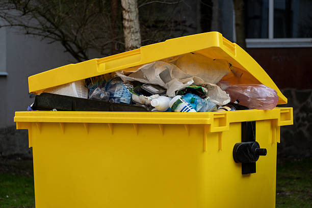 istock Yellow trash bin overflows with assorted waste materials in an outdoor setting, highlighting issues related to litter and waste disposal in urban areas 2207704991