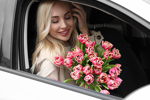 istock Happy young woman with beautiful bouquet in car 2207711032