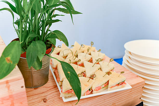 Neatly arranged triangle tea sandwiches with salmon and cucumber filling, secured with picks, ready to be served on white tray.