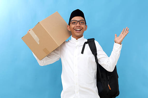 istock Excited asian muslim man carrying backpack and cardboard while raising hands hand,surprised gesture. Going mudik or travel to hometown for Ramadan eid mubarak celebration 2207720085