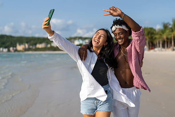 istock Happy interracial couple taking selfie at a tropical beach enjoying vacation, remote work 2207730107