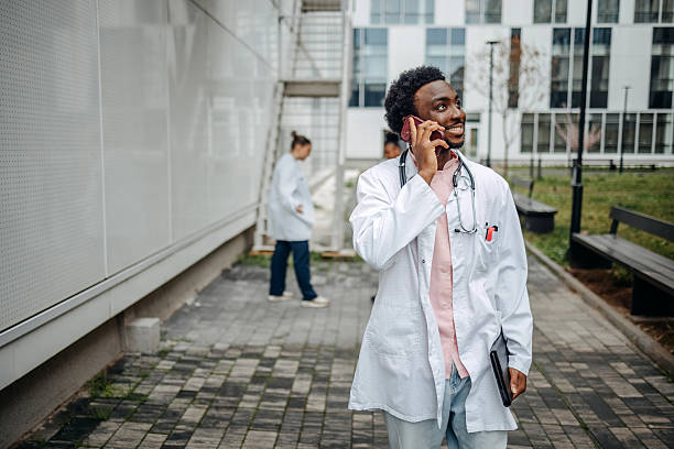 Mature senior man doctor talk on mobile phone in front hospital