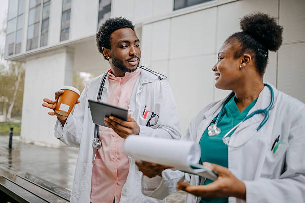 istock Young doctors having coffee break together outdoors in front of clinic and talking about work using digital tablet 2207731365