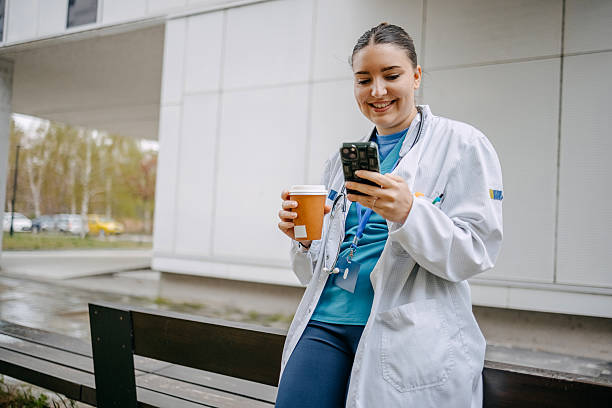 istock Young female doctor having coffee break outdoors in front of clinic using mobile phone 2207731487