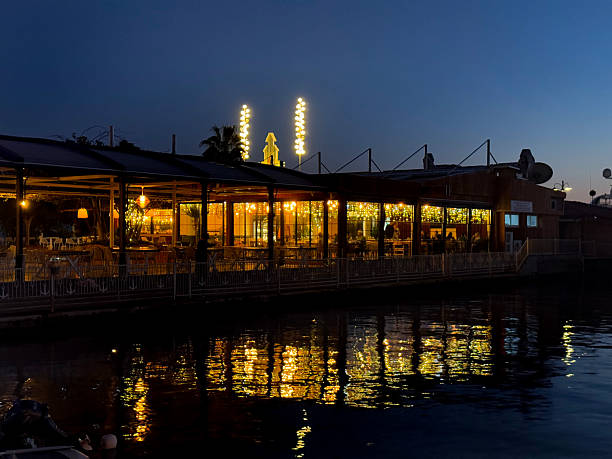 London, UK - 17 November, 2023: people walk past an inviting, illuminated restaurant in the Battersea area of London, UK. The lights of the establishment are reflected in a water feature in the foreground.