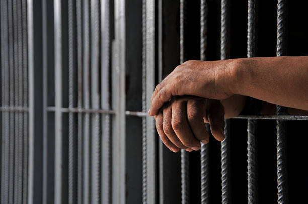 istock prisoner's hands behind bars with black background 2207734291