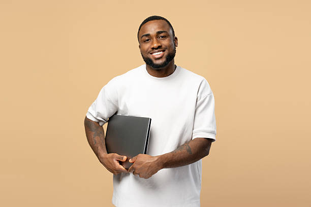 istock Smiling African American man holding laptop on beige background 2207737480
