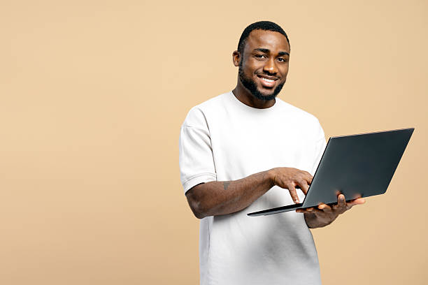 istock Smiling African American man using laptop on beige background 2207737508