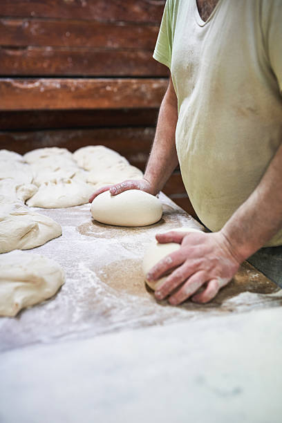 istock Baker forming dough into loaves on wooden floured table 2207738350
