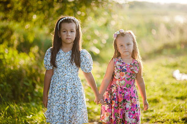 Cute girls and beautiful nature. Two little girls in floral dresses stand in the midst of nature. The white headband perfectly complements the delicate look of the younger sister.
