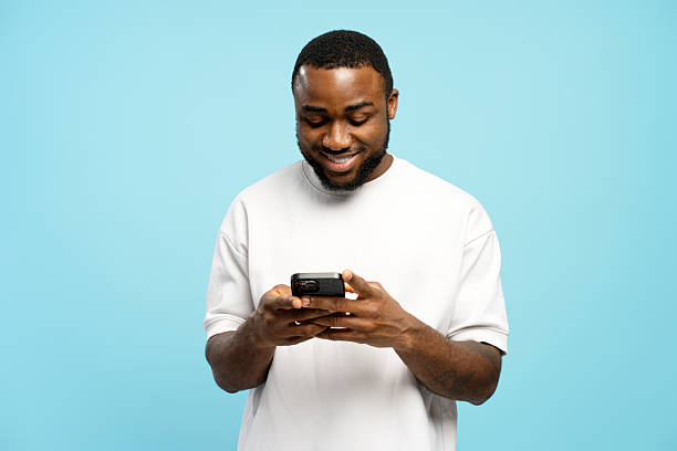 istock Smiling young African American man using smartphone on blue background 2207741834