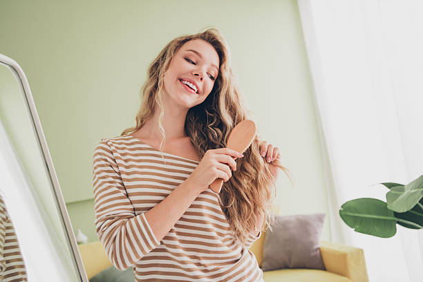 istock Young woman enjoying a relaxing weekend at home with a big smile in her striped pullover, brushing her beautiful blond hair in a bright living room. 2207742332