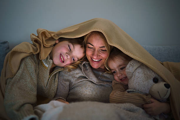 istock Woman and her children looking at mobile phone while sitting under the blanket 2207743176